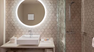 Un baño moderno con un espejo redondo, lavamanos blanco y ducha.