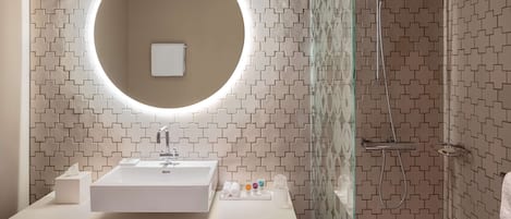 Un baño moderno con un espejo redondo, lavamanos blanco y ducha.