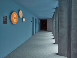 Un pasillo con paredes azules, luminarias circulares y piso alfombrado.