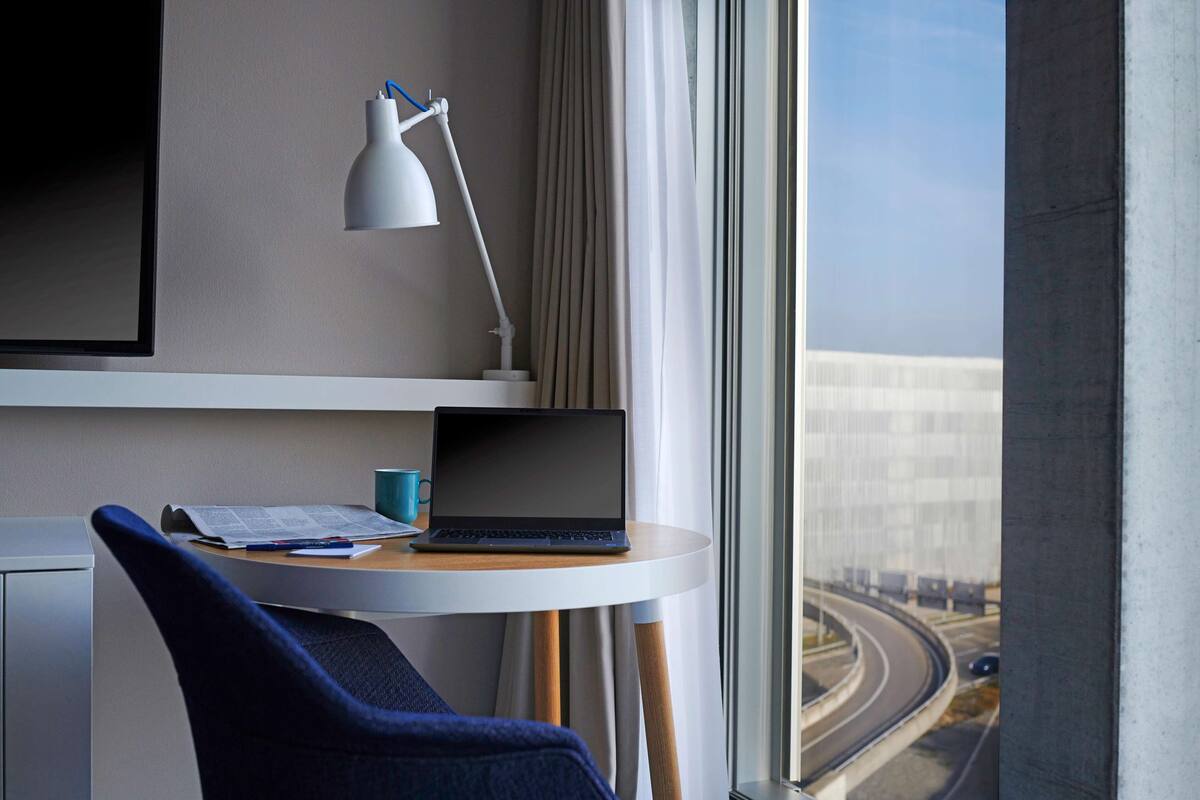 A hotel room with a desk, laptop, and a view of a highway through the window.