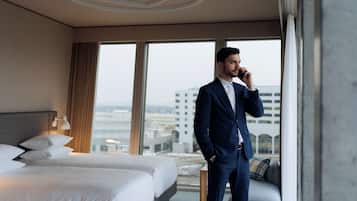 Ein Hotelzimmer mit einem großen Bett, einer Couch und Blick auf die Stadt durch große Fenster.