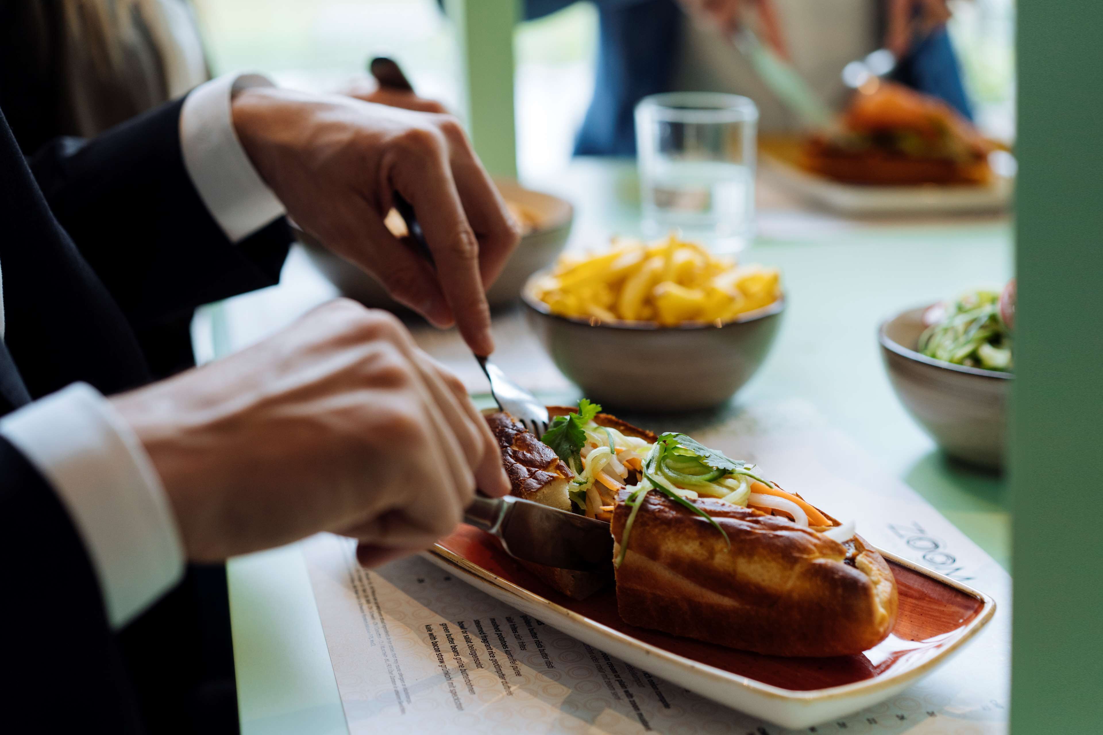 A person cutting a sandwich on a plate with a fork and knife.