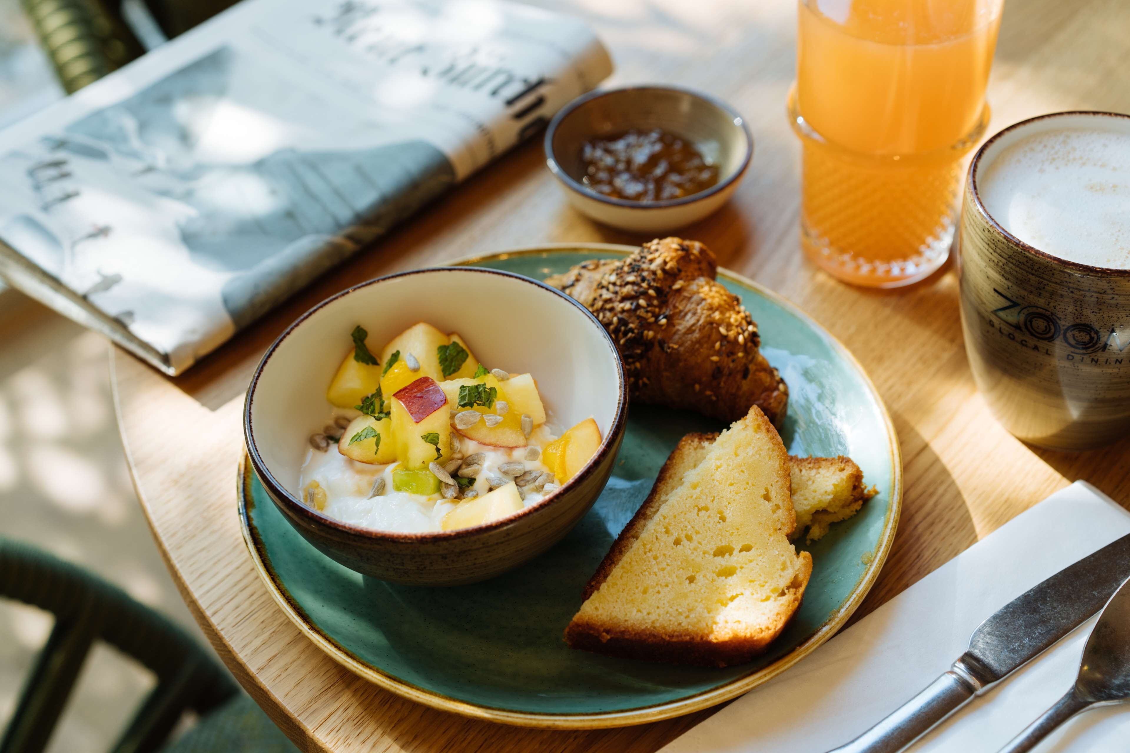 A meal with a bowl of fruit salad, a slice of bread, and a glass of orange juice on a table.