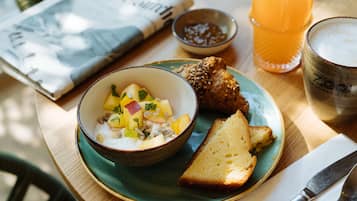 A meal with a bowl of fruit salad, a slice of bread, and a glass of orange juice on a table.
