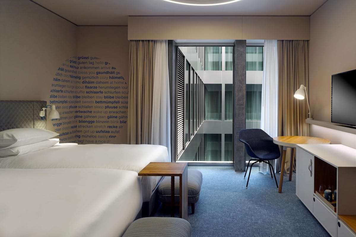 A modern hotel room with a bed, a desk, a chair, a TV, and a wall with text.