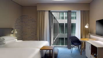A modern hotel room with a bed, a desk, a chair, a TV, and a wall with text.