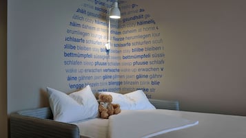 A bed with white bedding and a teddy bear, a wall with text in a foreign language, and a hanging light fixture.