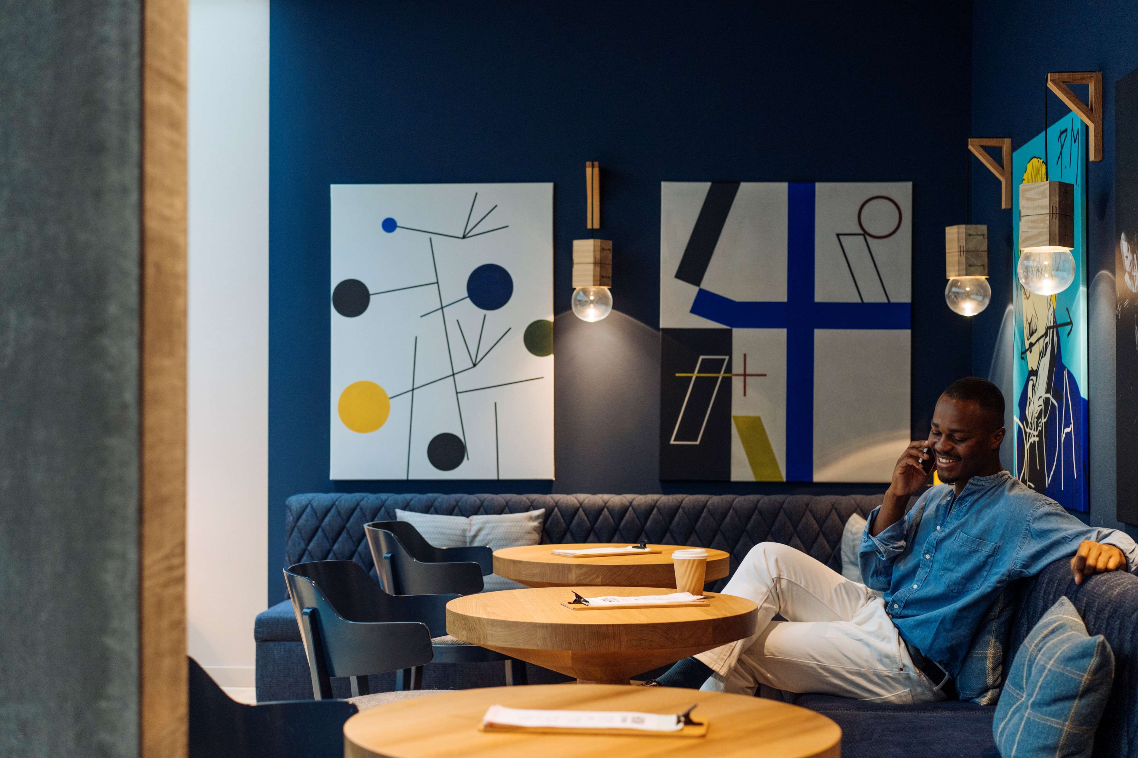 A modern lounge area with a blue sofa, round wooden tables, and abstract wall art.
