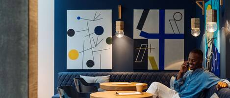 Un área de estar moderna con un sofá azul, mesas redondas de madera y arte abstracto en la pared.