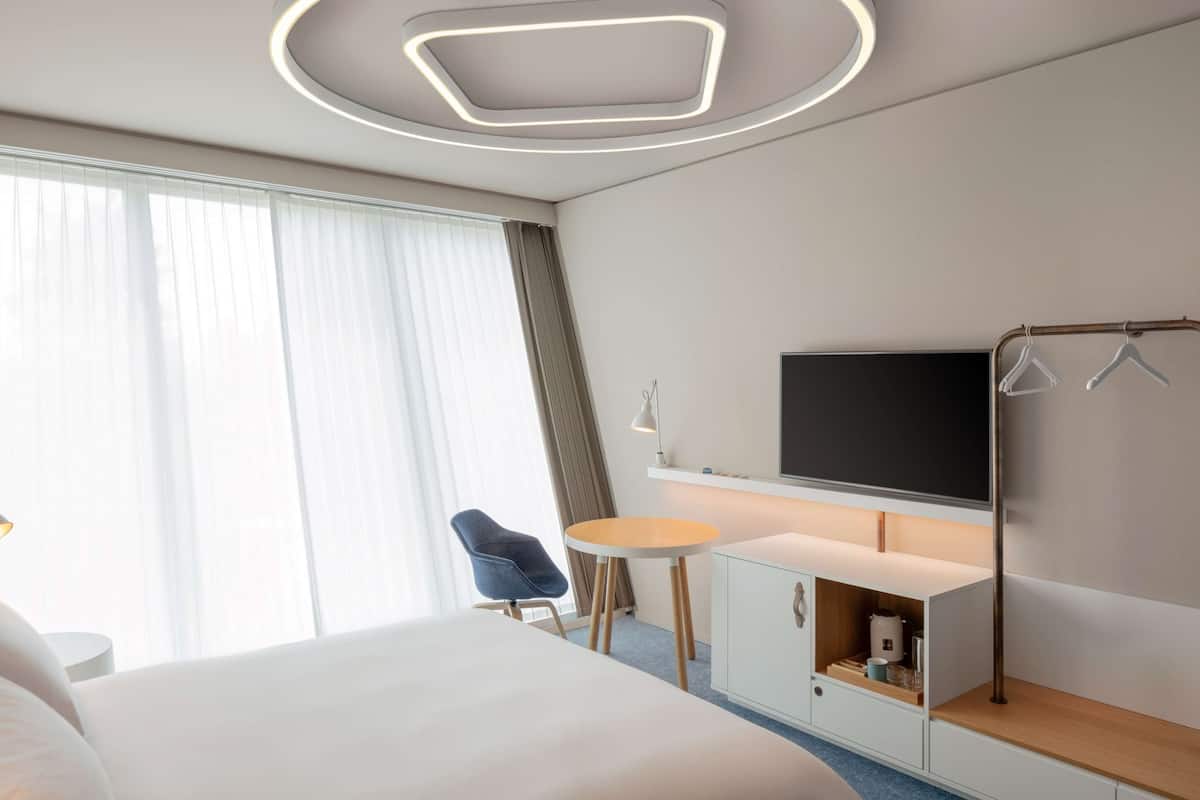 A modern hotel room with a large bed, a small round table, a TV, and a wardrobe.