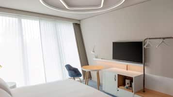 A modern hotel room with a large bed, a small round table, a TV, and a wardrobe.