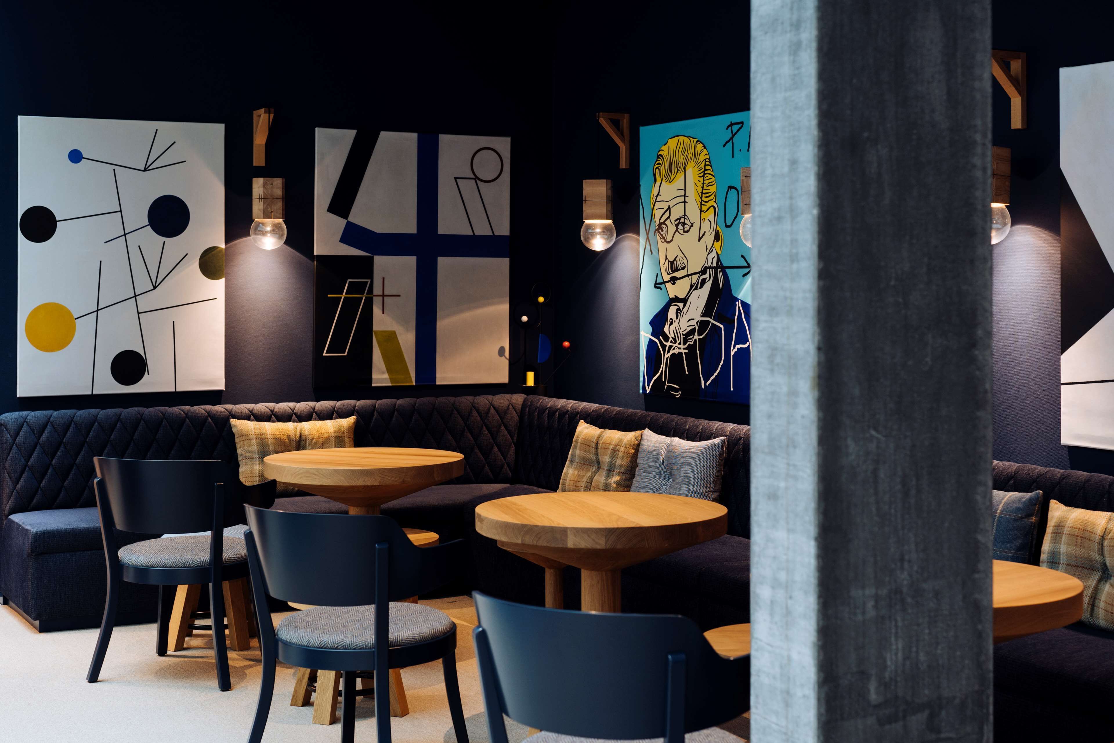 A modern lounge area with a dark-colored sofa, round wooden tables, and blue chairs.
