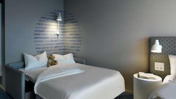 A neatly made bed with white linens, a teddy bear, and a wall with text in a foreign language.