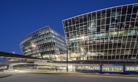 A modern building with large glass windows and a train station in the foreground.