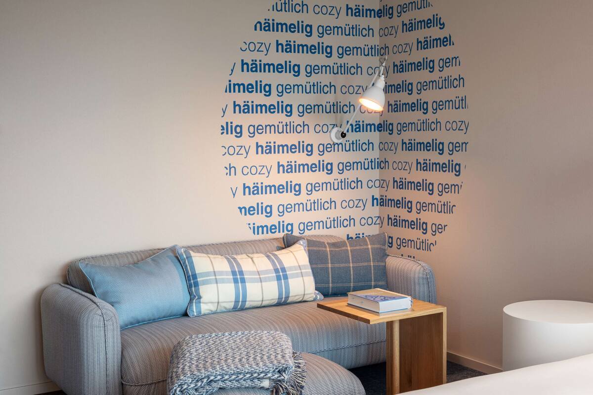 A modern living room with a sofa, pillows, a small table with a book, and a wall with text.