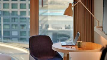 Ein modernes Hotelzimmer mit Blick auf eine Stadtlandschaft, ein runder Tisch mit Laptop und Tasse sowie ein Sessel.