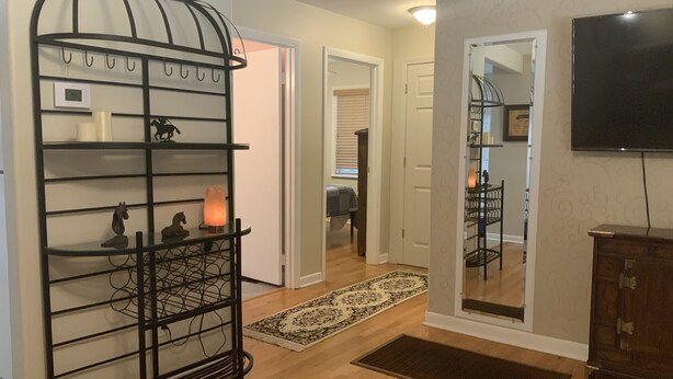 A hallway with a black metal rack, a rug, a wooden cabinet, and a TV mounted on the wall. - Clean Cozy Bungalow on THE BACK STRETCH Close to Oaklawn Racing and Casino (Hot Springs)