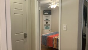 A narrow hallway leading to a bedroom with a bed, a ceiling fan, and a shelf with decorative items. - Clean Cozy Bungalow on THE BACK STRETCH Close to Oaklawn Racing and Casino (Hot Springs)