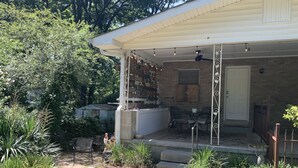A covered patio area with a brick wall, outdoor furniture, and a small garden. - Clean Cozy Bungalow on THE BACK STRETCH Close to Oaklawn Racing and Casino (Hot Springs)