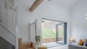 A modern interior with a staircase, a wooden beam, a glass door leading to an outdoor area, and a small table with a lamp. - Brook Cottage - 7 Bedroom Cottage - Dale (Haverfordwest)