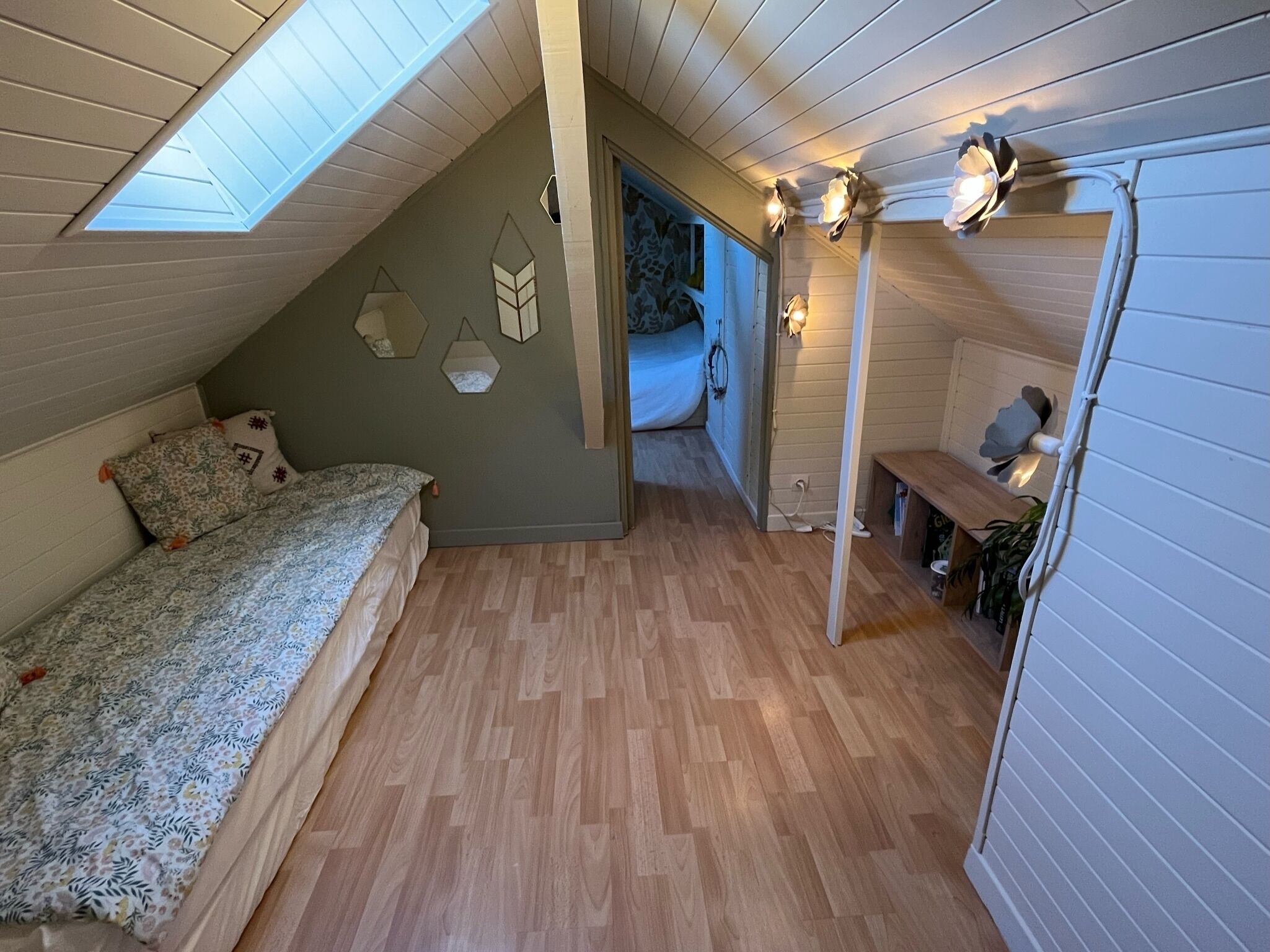 Een slaapkamer met een schuine kap, een bed, een bankje en een dakraam.