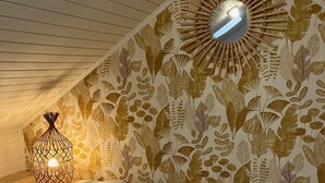 Una habitación con techo inclinado, pared con diseño, lámpara colgante y una cama.