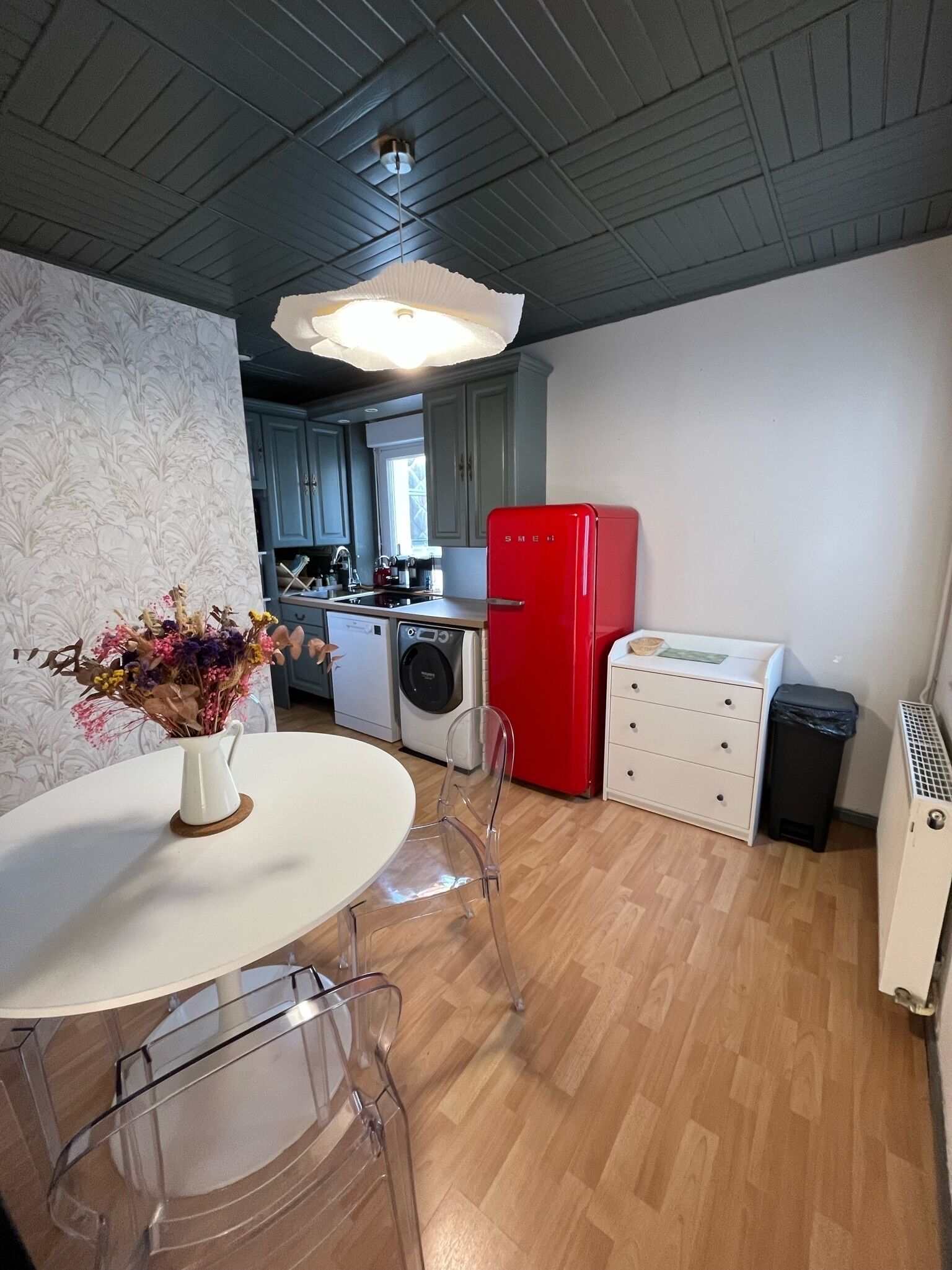 Une cuisine compacte avec un réfrigérateur rouge, un lave-linge et un coin repas comprenant une table et des chaises.
