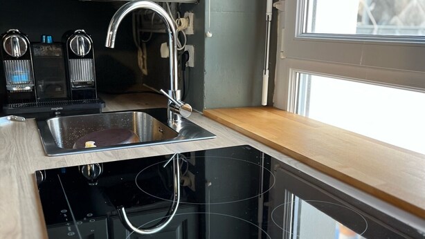 Una cocina con estufa negra, pileta de acero inoxidable y ventana con vista.