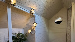 Habitación con paredes de madera, techo inclinado y suelo de madera. Hay tres luces fijadas a la pared y una planta en maceta a la izquierda.