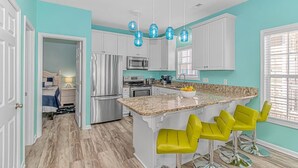 A modern kitchen with white cabinets, a granite countertop, and a central island with yellow bar stools. - COCONUT TREEHOUSE, 5 bed/3.5 bath, 1 minute walk to beach, Holiday Inn section (Myrtle Beach)