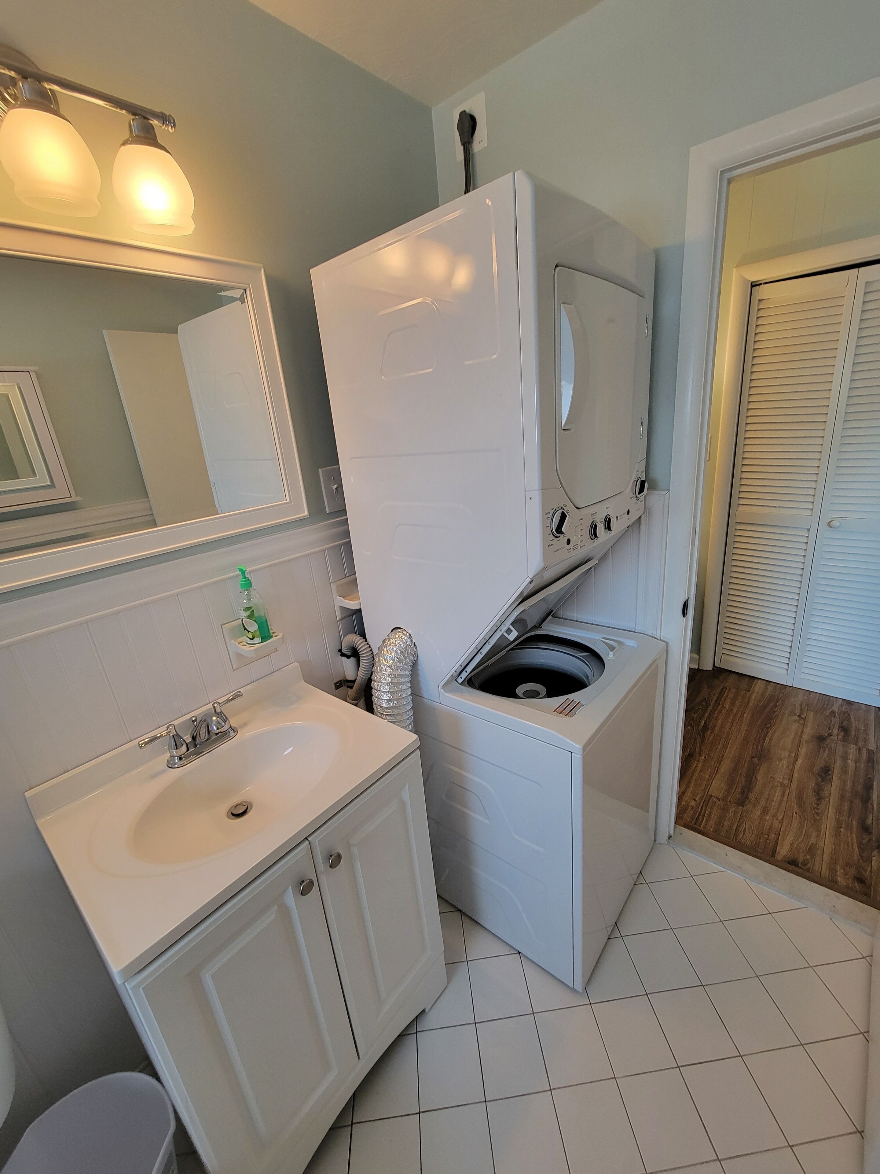 A compact bathroom with a white sink, mirror, and a built-in washer and dryer.