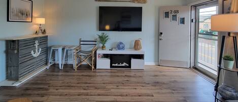 Una habitación con piso de madera, un escritorio con televisor, una silla, una lámpara y una puerta con un número.