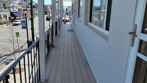 Ein überdachter Außenbalkon mit Holzboden, Metallgeländer und großen Fenstern.