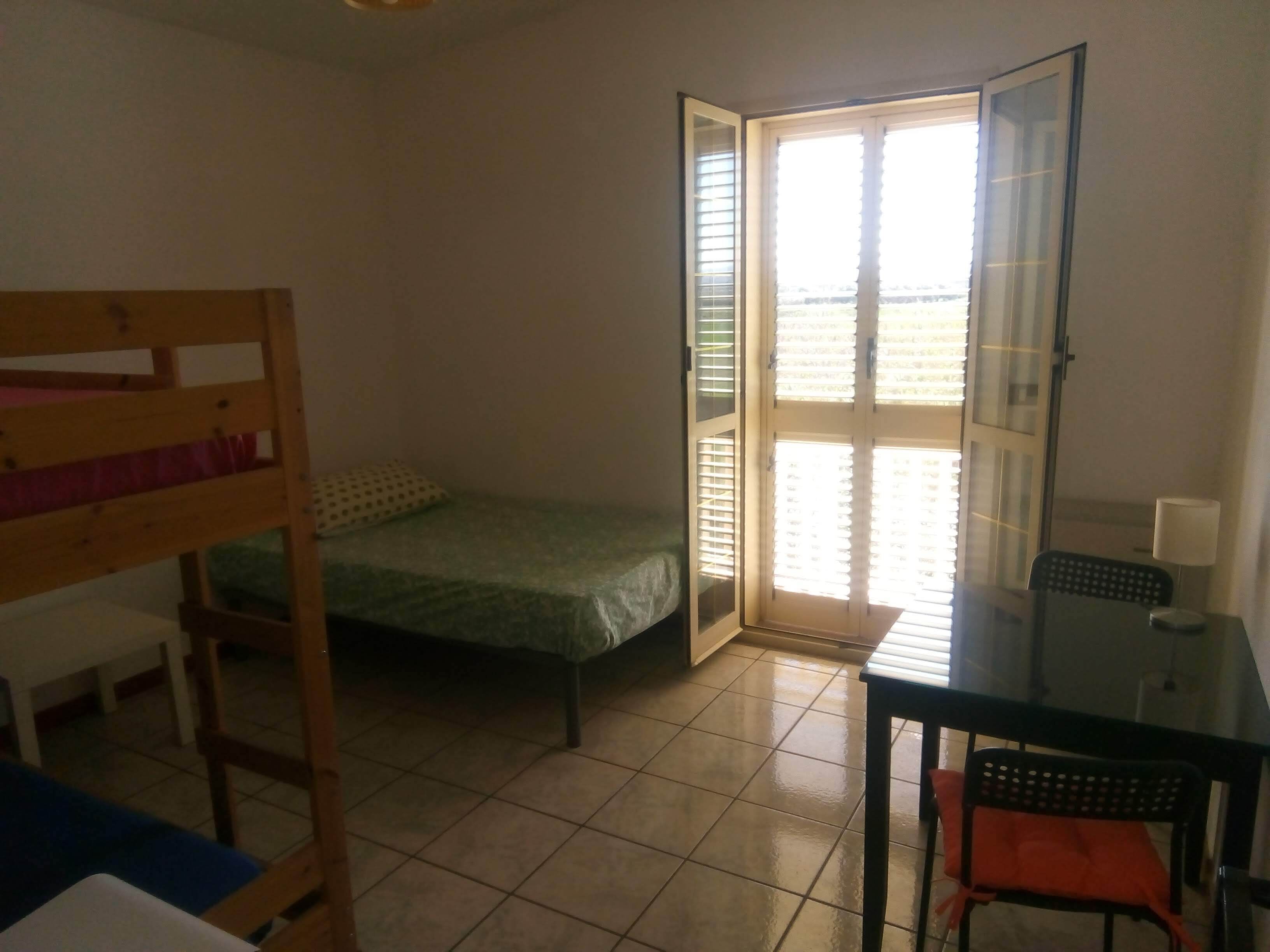 Une chambre avec un lit superposé, une petite table avec une chaise et une porte-fenêtre coulissante donnant sur un espace extérieur.
