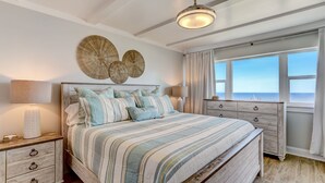 A bedroom with a large bed, two bedside tables, a ceiling fan, and a window with a view. - Oceanfront Penthouse | Renovated Bathrooms | Exclusive Amelia by the Sea Pier Access (Fernandina Beach)