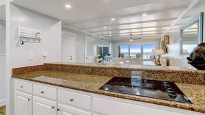 A kitchen with granite countertops, white cabinetry, and a built-in stovetop. - Oceanfront Penthouse | Renovated Bathrooms | Exclusive Amelia by the Sea Pier Access (Fernandina Beach)