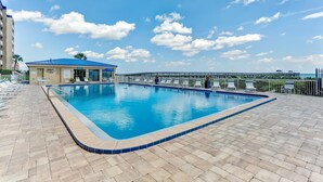 A swimming pool with a blue tiled edge, lounge chairs, and a building with a blue roof. - Oceanfront Penthouse | Renovated Bathrooms | Exclusive Amelia by the Sea Pier Access (Fernandina Beach)