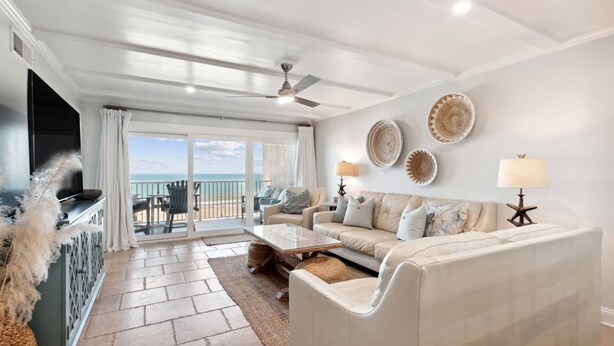 A spacious living room with a large sofa, a coffee table, and a TV. There is a balcony with a view of the ocean. - Oceanfront Penthouse | Renovated Bathrooms | Exclusive Amelia by the Sea Pier Access (Fernandina Beach)