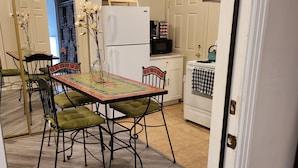 A dining area with a table set for four, surrounded by chairs with green cushions. A white refrigerator and a microwave are visible in the background. - PRIVATE OASIS-MONTHLY RENTAL/ POOL/SPA/GOLF/WIFI/PARKING/REVIEWS! (Las Vegas)