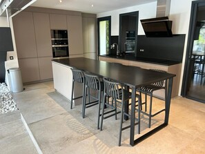 A modern kitchen with a central island, built-in appliances, and a dining area with bar stools.