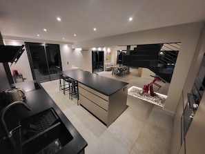 A modern kitchen with a central island, dining area with chairs, and a staircase. - VILLA BEL AIR CANNES - NEW - Pool - No Party allowed - No bachelor-ette stay (Le Cannet)