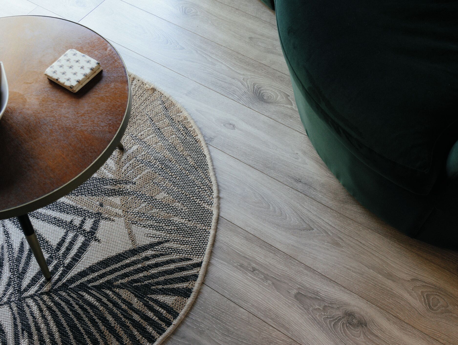A round table with a woven rug, a small square object on the table, and a green upholstered sofa.