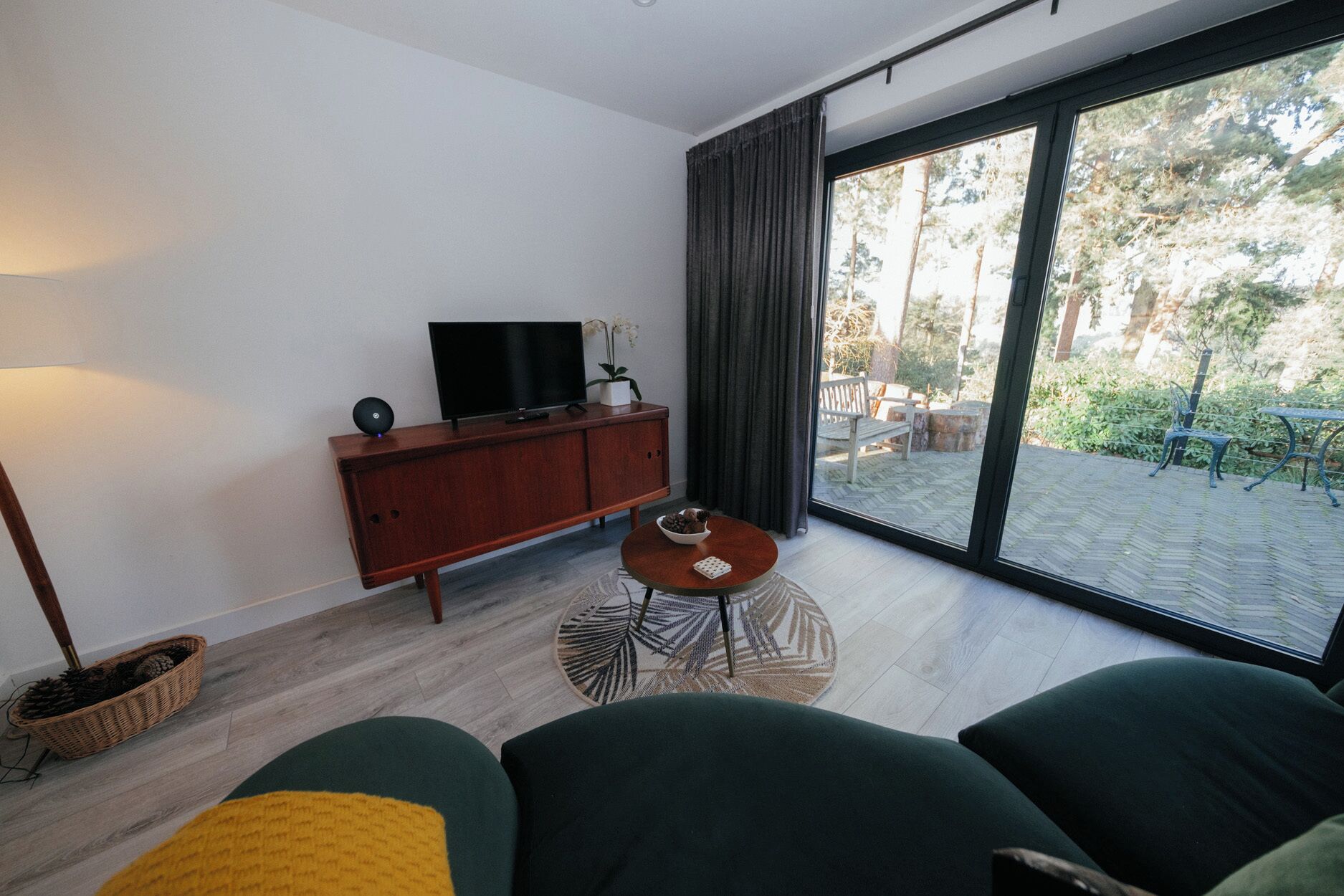 A modern living room with a large window, a flat-screen TV, a wooden cabinet, and a round coffee table.