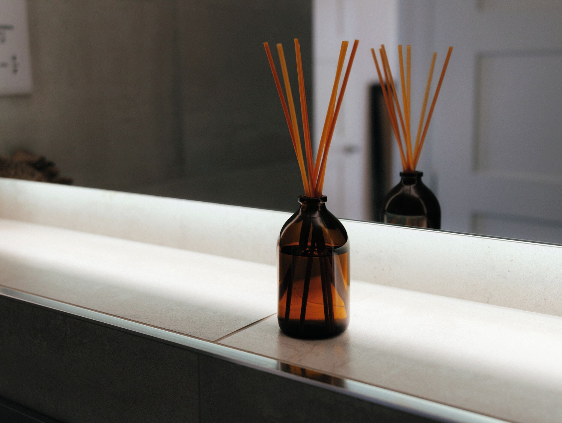 Un petit vase marron avec des tiges de roseau, posé sur un comptoir blanc.