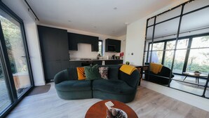 A modern living room with a dark green sectional sofa, a wooden coffee table, and a large window with a view of greenery. - The Observatory Annexe (Dorking)