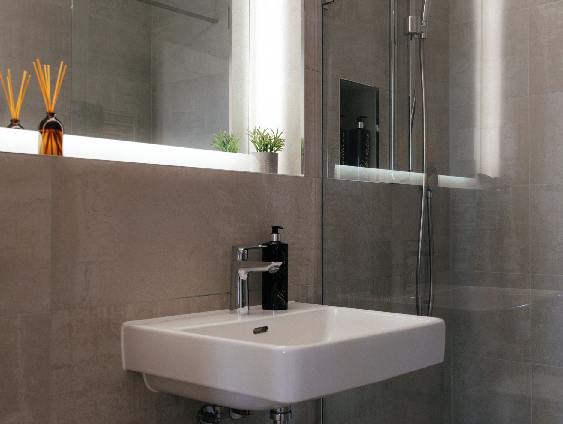 Une salle de bain moderne avec un lavabo blanc, une cabine de douche en verre et un miroir au-dessus du lavabo.