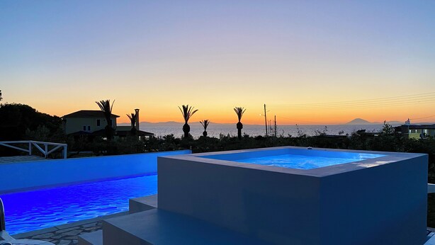 Un espace piscine extérieur moderne offrant une vue sur la mer au coucher du soleil.