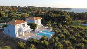 Une maison à deux étages avec une piscine, entourée de verdure et offrant une vue sur la côte.