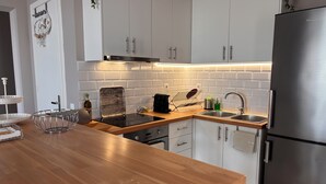 Une cuisine moderne avec des meubles blancs, un réfrigérateur en acier inoxydable, un plan de travail en bois et un four encastré.
