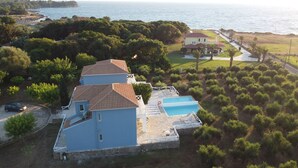 Une grande maison avec une piscine, entourée d’arbres et offrant une vue sur la mer.
